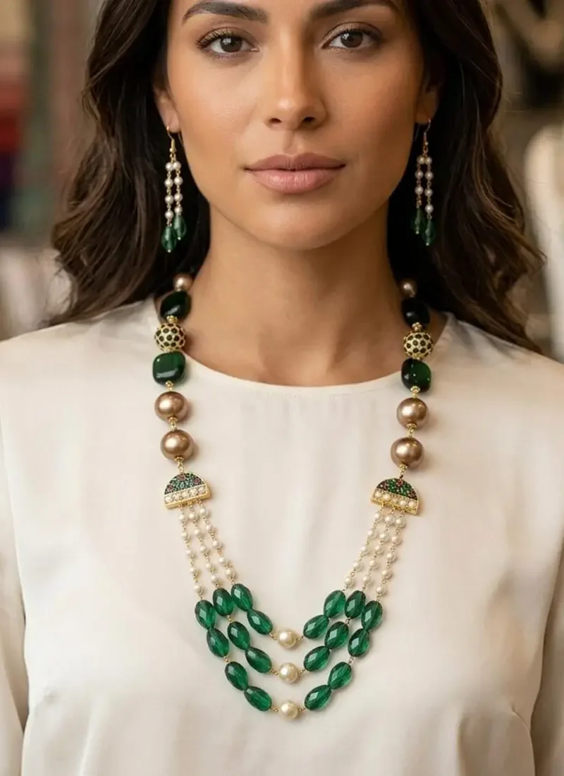 Layered faux pearl necklace featuring green crystals, dual meenakari pendants, and golden ball accents with matching earrings